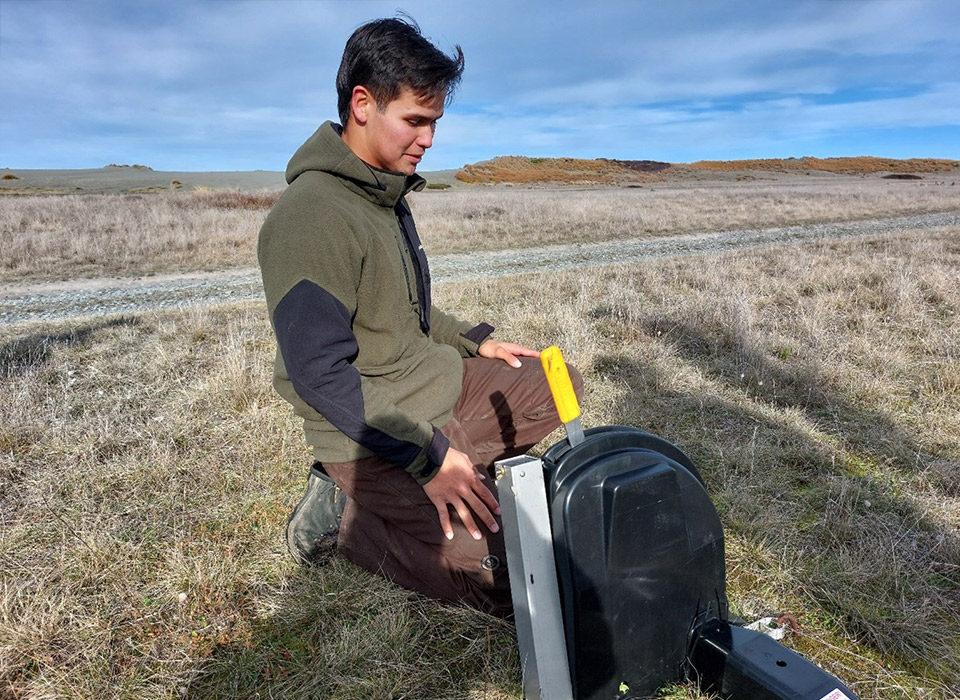 A man kneels down in front of a podiTRAP, a rounded black box with a yellow lever