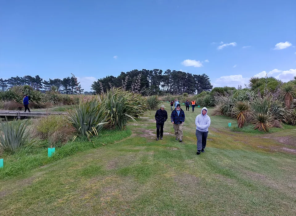 Three people walk along the Te Waikēkēwai stream